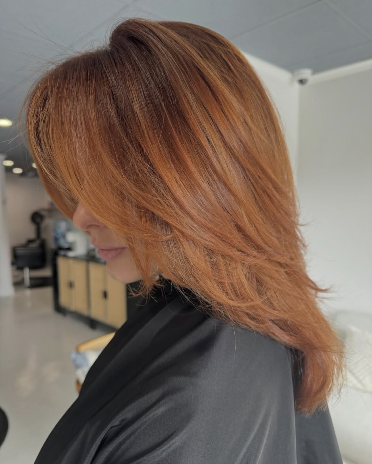 Side profile of a woman with medium-length, layered copper red hair in a hair salon setting